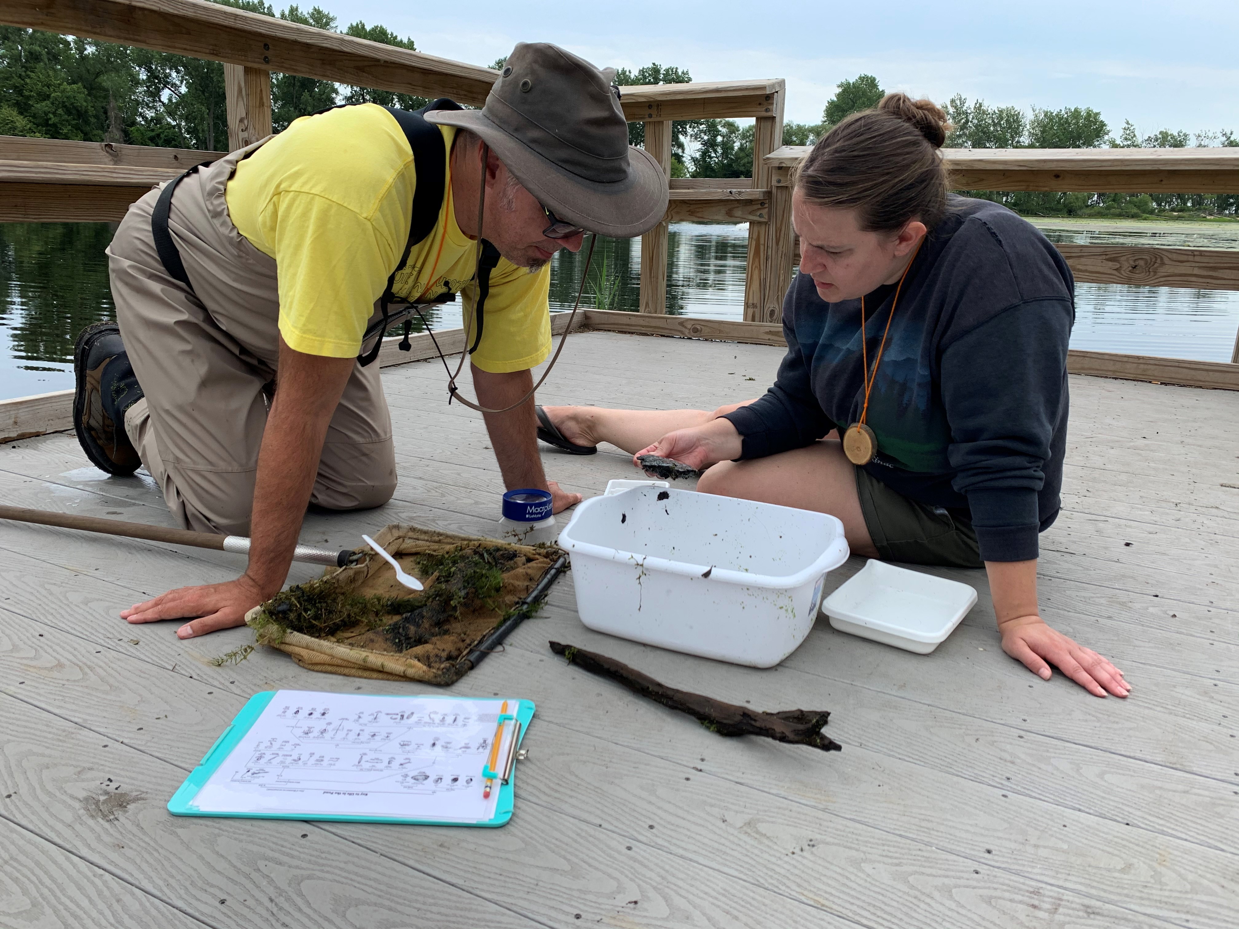 Two people kneeling and sitting on a dock examine water samples.